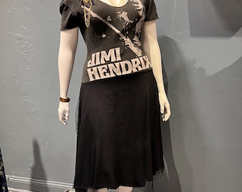 May include: A mannequin wearing a black outfit. The outfit features a black t-shirt with the text "Jimi Hendrix" and an image of the musician. The t-shirt is paired with a black skirt. A gold necklace and bracelet are also visible.