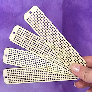 May include: Four wooden craft strips with evenly spaced holes, held against a purple background. Each strip is rectangular with rounded ends and a single hole at one end. The strips are a light, natural wood color.