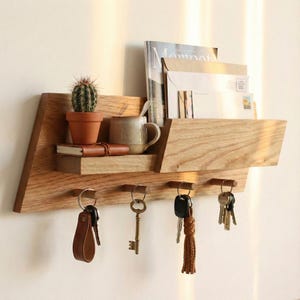 以下が含まれることがあります： 木製の壁掛けオーガナイザー。棚、キーフック、雑誌ホルダー付き。 棚には、テラコッタの鉢植えの小さなサボテン、マグカップ、小さなノートが入っています。 キーは下のフックから吊り下げられています。