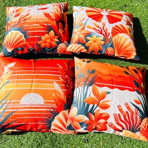 May include: Four square cushions with a vibrant sunset and ocean-themed design. The cushions feature orange, red, and white colours with seashell, floral, and plant illustrations. The cushions are placed on a green grassy surface.
