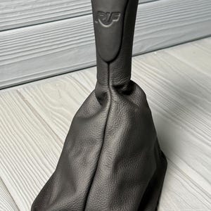 May include: A black gear shift knob and boot. The knob has the numbers 1, 2, 3, 4, 5, and 6, and the letters "R" and "F" are visible. The boot is made of a textured material.
