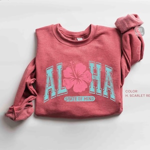 May include: A scarlet red sweatshirt with the word "ALOHA" in light blue block letters and a pink hibiscus flower in the center. The words "STATE OF MIND" are below the flower. The sweatshirt has long sleeves.