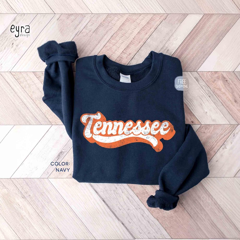 May include: Navy blue sweatshirt with the word "Tennessee" in orange and white retro lettering. The sweatshirt has a crew neck and long sleeves. The color of the sweatshirt is navy.