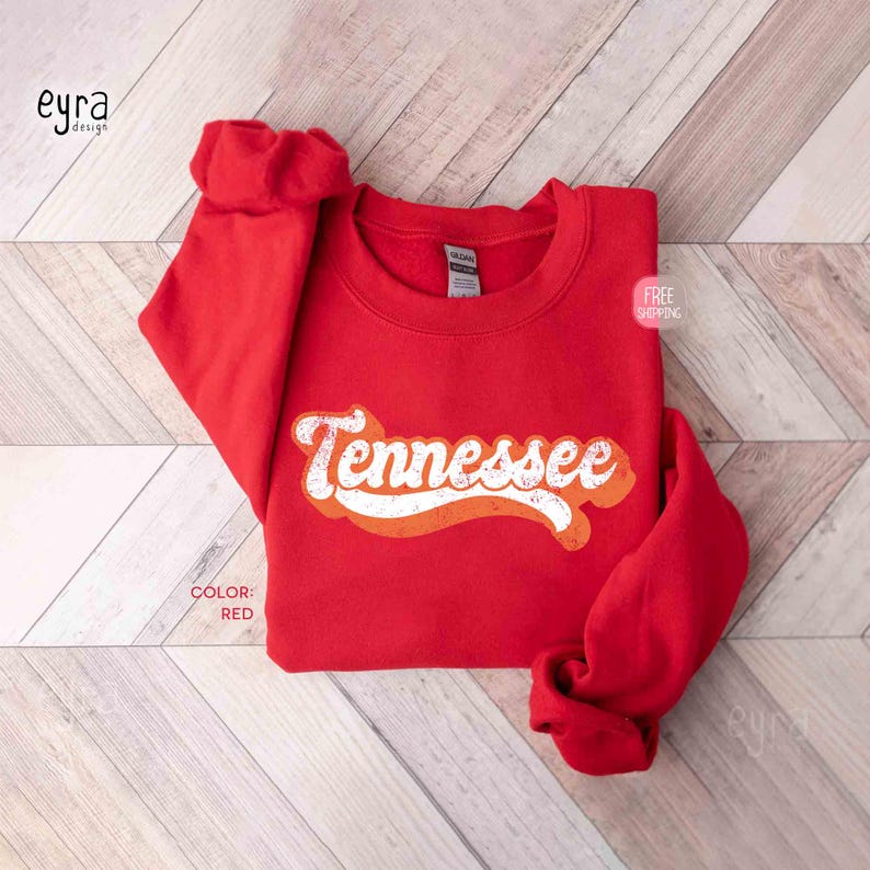 K&ouml;nnte beinhalten: Ein leuchtend rotes Sweatshirt mit Rundhalsausschnitt und dem Wort Tennessee in wei&szlig;er, abgenutzter Schreibschrift auf der Brust. Das Kleidungsst&uuml;ck hat lange &Auml;rmel und einen gerippten Kragen sowie ein sichtbares Markenetikett am Halsausschnitt.