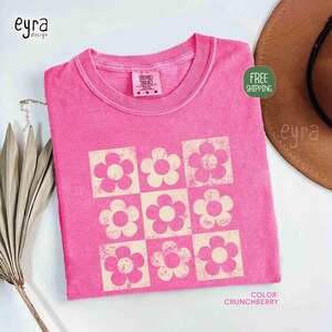 May include: A pink t-shirt with a retro floral design. The shirt features a grid of nine flowers in a lighter shade of pink. The text "COLOR: CRUNCHBERRY" is visible. The shirt is a medium size.