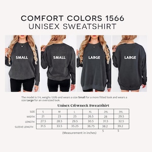 May include: A Comfort Colors 1566 unisex crewneck sweatshirt in dark gray. The image shows the back of the sweatshirt on models wearing sizes Small and Large. A size chart provides measurements in inches for sizes S to 3XL.