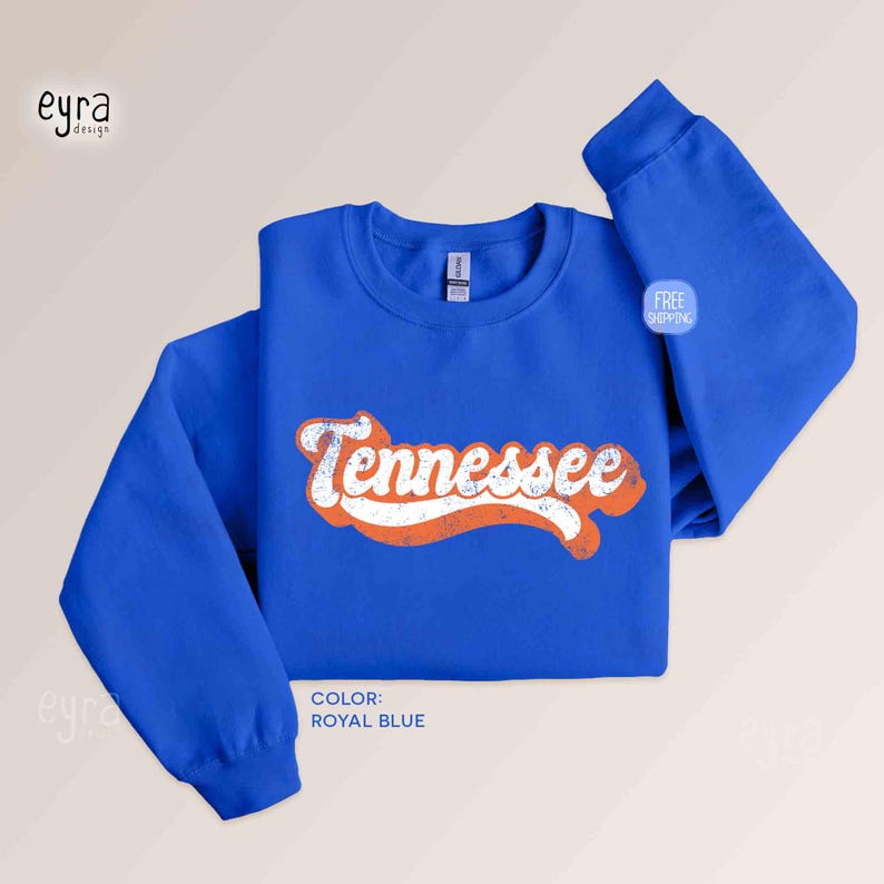 K&ouml;nnte beinhalten: Ein k&ouml;nigsblaues Langarm-Sweatshirt mit Rundhalsausschnitt und dem Wort Tennessee in wei&szlig;er, abgenutzter Schreibschrift mit orangefarbener Umrandung. Das Kleidungsst&uuml;ck hat einen gerippten Kragen, B&uuml;ndchen und Saum sowie ein sichtbares Etikett.