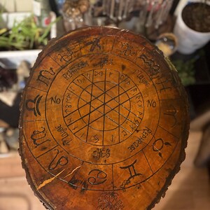 May include: A round, wooden divination board with a dark brown finish. The board features etched zodiac symbols, runes, and the words "Yes", "No", and "Maybe". A tree design is at the bottom.