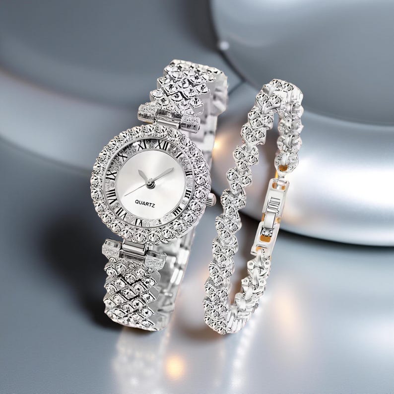 May include: A silver-toned quartz watch and matching bracelet set. The watch features a round face with Roman numeral hour markers and a bezel encrusted with sparkling crystals. The bracelet has a similar crystal design.