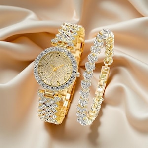 May include: A gold-toned watch and bracelet set. The watch features a round face with a crystal-studded bezel and a matching band. The bracelet has a heart-shaped design. Both pieces are set against a satin background.