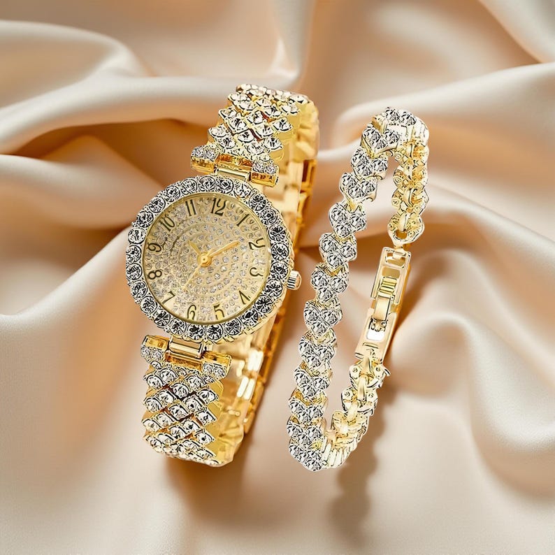 May include: A gold-toned watch and bracelet set. The watch features a round face with a crystal-studded bezel and a matching band. The bracelet has a heart-shaped design. Both pieces are set against a satin background.