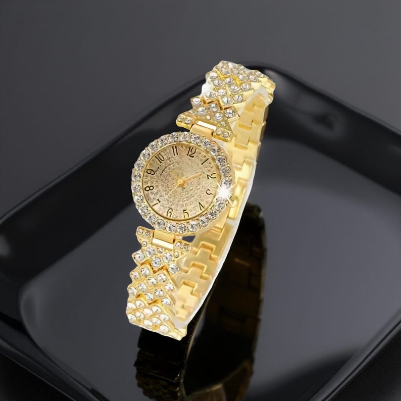 May include: A gold-toned wristwatch with a round face and a sparkling bezel. The watch features a textured dial and is adorned with numerous small, clear crystals. The band is also gold-toned and embellished with crystals, creating a glamorous look.
