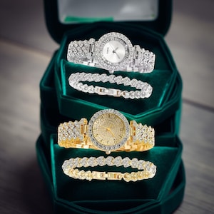 May include: Two watches and two bracelets displayed in a green velvet box. One watch is silver-toned with a white face and crystal accents. The other is gold-toned with a gold face and crystal accents. Both watches and bracelets have crystal embellishments.