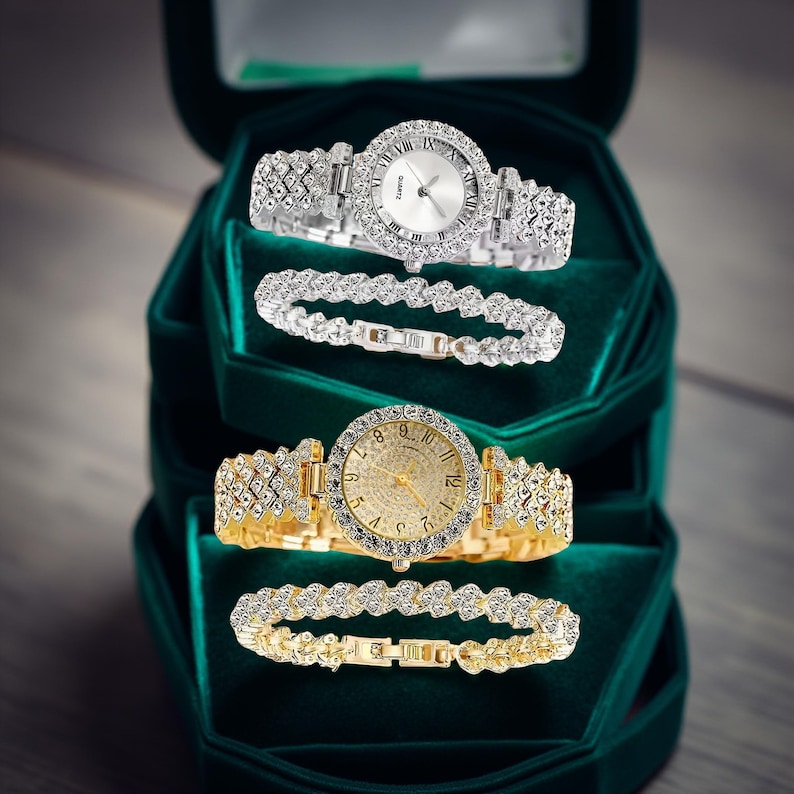 May include: Two watches and two bracelets displayed in a green velvet box. One watch is silver-toned with a white face and crystal accents. The other is gold-toned with a gold face and crystal accents. Both watches and bracelets have crystal embellishments.