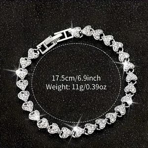 May include: A silver bracelet featuring heart-shaped links, each encrusted with small, sparkling crystals. The bracelet is 6.9 inches long and weighs 0.39 ounces. The clasp is visible, and the bracelet is displayed on a dark surface.