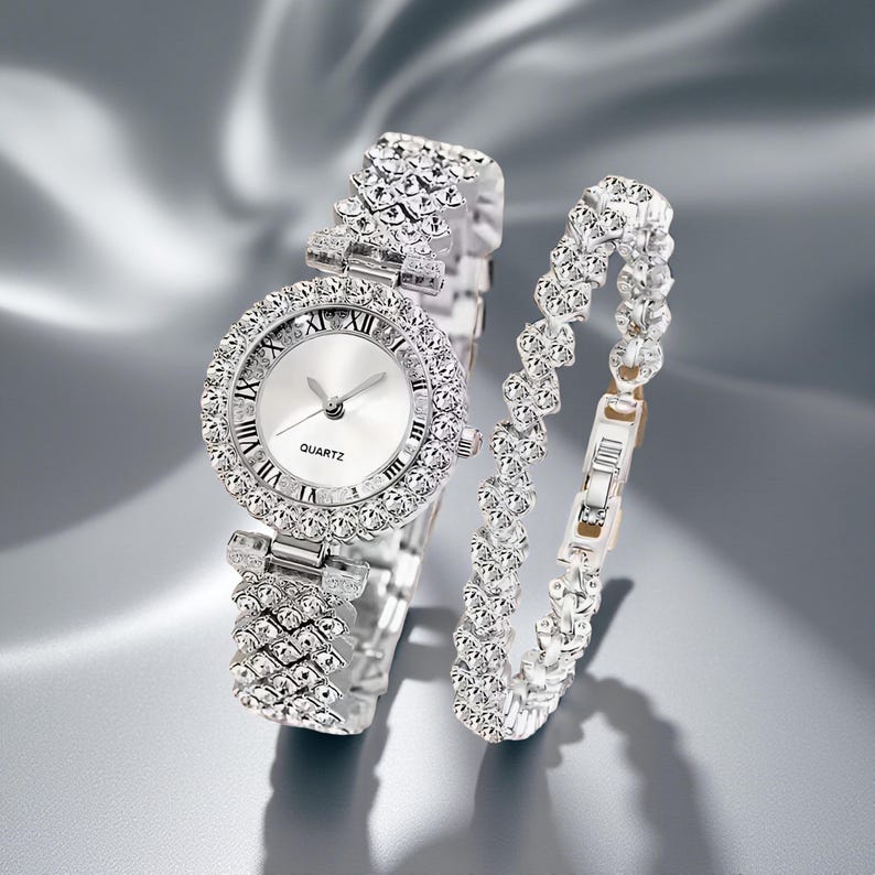 May include: A silver-toned quartz watch and matching bracelet set. The watch features a round face with Roman numeral hour markers and a bezel encrusted with sparkling crystals. The bracelet has a similar design, with a series of crystal-studded links.