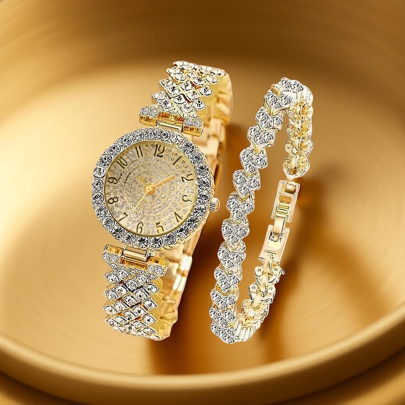 May include: A gold-toned watch and bracelet set. The watch features a round face with a crystal-studded bezel and a crystal-covered dial. The watch band and bracelet are also adorned with crystals. The bracelet has a heart-shaped design.