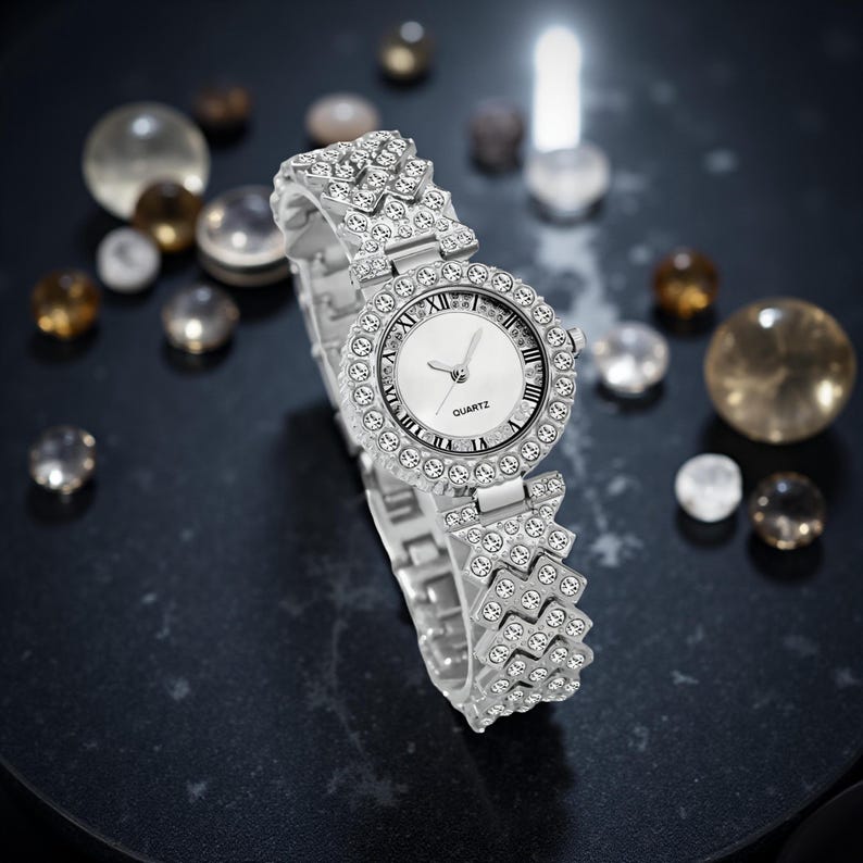 May include: Silver-toned quartz watch with a white face and Roman numeral hour markers. The watch is encrusted with clear crystals around the bezel and on the band. The word "QUARTZ" is printed on the watch face.