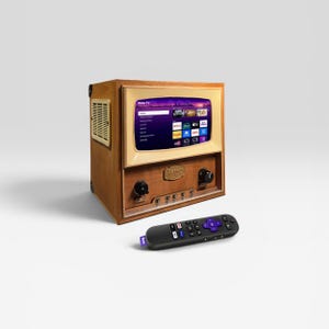 Può includere: Un televisore in stile retrò con un mobile in legno marrone chiaro e una cornice dello schermo color crema. Lo schermo mostra un'interfaccia di servizio di streaming. Un telecomando nero con accenti viola è davanti.