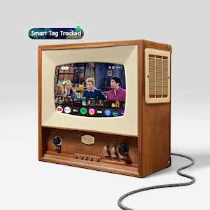 Könnte beinhalten: Ein hölzernes Fernsehgerät mit cremefarbenem Bildschirmrahmen und seitlichem Lautsprechergitter. Der Bildschirm zeigt eine Benutzeroberfläche mit verschiedenen Streaming-App-Symbolen. Ein schwarzes Netzkabel ragt aus der Basis. Etikett Smart Tag Tracked.