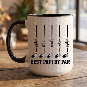 May include: White ceramic coffee mug with a black handle and rim. The mug features a golf-themed design with the text "BEST PAPI BY PAR" and names. The design includes golf clubs and names: Sophia, Ethan, Emily, Jackson, and Sophia.