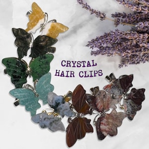May include: A collection of crystal butterfly hair clips in various colors, including green, blue, brown, and yellow. The clips are arranged in a circular pattern, with the text "CRYSTAL HAIR CLIPS" in purple. A sprig of lavender is in the background.