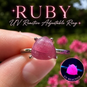 May include: An adjustable ring featuring a triangular, cabochon-cut pink gemstone set in a silver-toned metal band. The text RUBY UV Reactive Adjustable Ring is displayed above, and a circular inset shows the stone glowing bright pink under UV light.