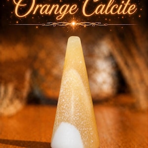 K&ouml;nnte beinhalten: Ein kegelf&ouml;rmiger Pr&auml;sentationsst&auml;nder aus orangefarbenem Calcit mit glatter, polierter Oberfl&auml;che. Der Stein zeigt durchscheinende goldorange Farbt&ouml;ne mit einem deutlichen, undurchsichtigen wei&szlig;en Fleck an der Basis. Der Text Orange Calcite steht dar&uuml;ber.