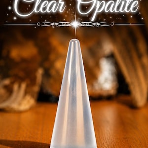 K&ouml;nnte beinhalten: Ein durchscheinender, kegelf&ouml;rmiger Ringst&auml;nder aus klarem Opalit. Das Objekt hat eine glatte, spitz zulaufende Oberfl&auml;che und einen runden Boden. Der Text "Clear Opalite" steht in wei&szlig;er Schreibschrift &uuml;ber dem Objekt mit Sternakzenten.