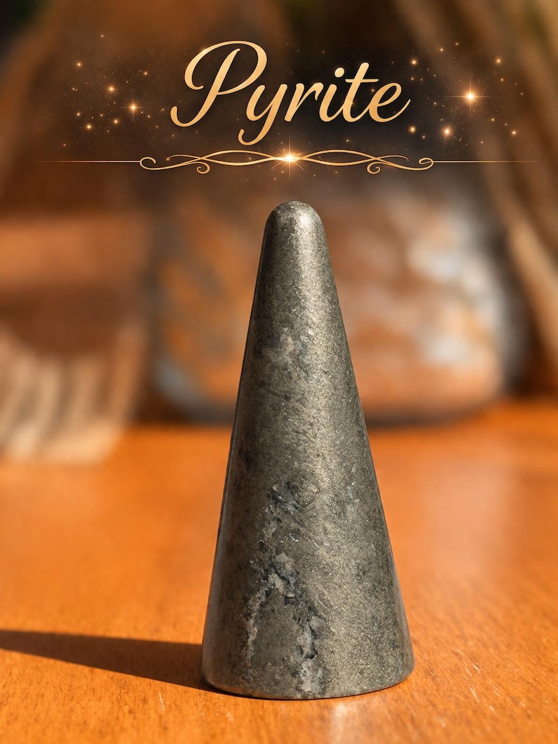 K&ouml;nnte beinhalten: Ein kegelf&ouml;rmiges Objekt aus metallisch grauem Pyrit mit einer glatten, polierten Oberfl&auml;che und sichtbaren nat&uuml;rlichen Mineraleinschl&uuml;ssen. Das Wort Pyrite ist in einer kursiven, goldfarbenen Schrift &uuml;ber dem Stein gedruckt, erg&auml;nzt durch kleine dekorative Funken.