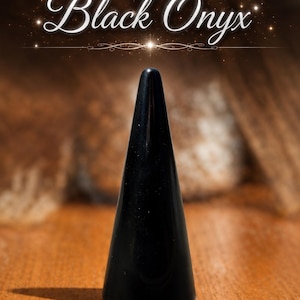 K&ouml;nnte beinhalten: Ein glatter, polierter schwarzer Onyxstein, der in eine hohe, schlanke Kegelform geschliffen ist. Die Oberfl&auml;che des Steins ist dunkel und reflektierend. &Uuml;ber dem Stein steht der Text Black Onyx in einer wei&szlig;en, eleganten Schreibschrift.
