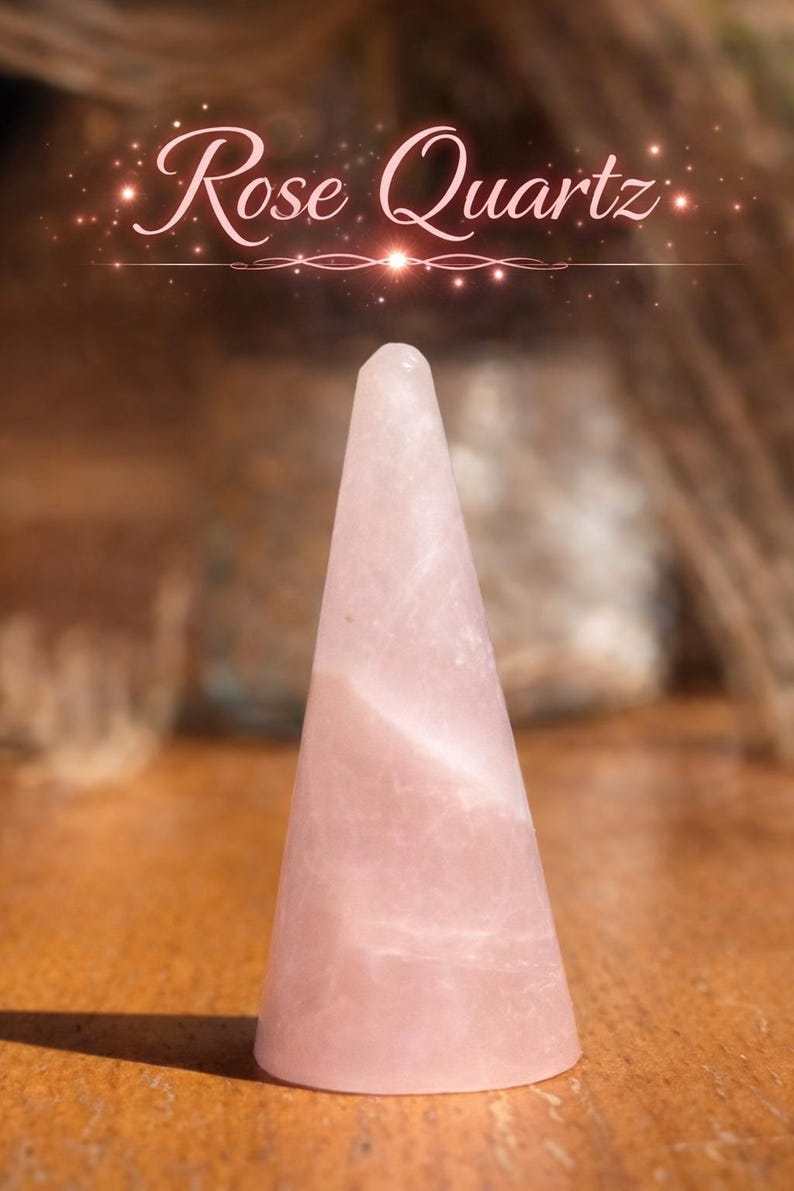 K&ouml;nnte beinhalten: Ein blassrosa Rosenquarzkristall, der in eine glatte, konische Form geschliffen ist. Der Stein weist nat&uuml;rliche interne Maserungen und ein halbtransparentes Aussehen auf. &Uuml;ber dem Kristall steht der Text Rose Quartz in wei&szlig;er Schrift.