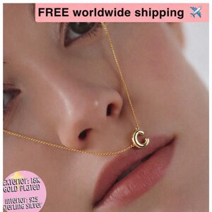May include: A gold-plated necklace with the letter "C" pendant. The necklace is displayed on a person's face. The exterior is 18K gold plated, and the interior is 925 sterling silver.