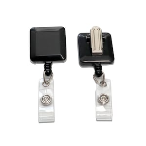 May include: Two black retractable badge holders with clear plastic straps and silver clips. One holder has a square badge holder and the other has a clip for attaching to clothing.