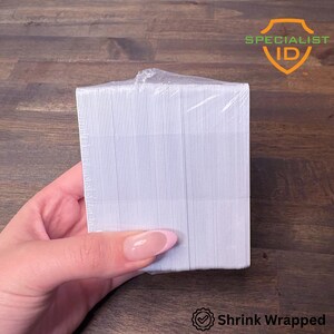 May include: A stack of white, vertically striped cards, shrink-wrapped in clear plastic. The cards are held by a hand with a pink manicure. The Specialist ID logo is visible in the upper right corner, and the words "Shrink Wrapped" are at the bottom.