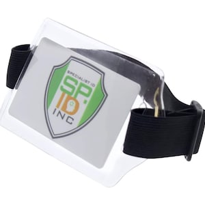 May include: A clear plastic ID badge holder with a black elastic wrist strap. The holder has a logo that says "Specialist ID SP. ID INC" with a green, yellow, and black shield design.
