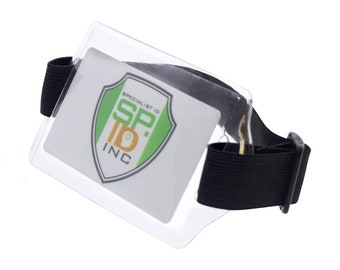 Puede incluir: Un porta-credencial de plástico transparente con una correa elástica negra para la muñeca. El porta-credencial tiene un logotipo que dice "Specialist ID SP. ID INC" con un diseño de escudo verde, amarillo y negro.