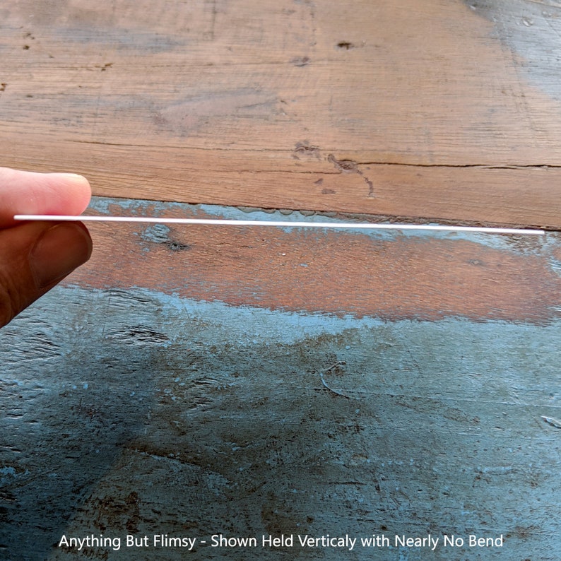 May include: A close-up of a white, rigid sheet of material held vertically. The sheet is held by a hand and shows no signs of bending or flexing. The caption below the sheet reads "Anything But Flimsy - Shown Held Vertically with Nearly No Bend".