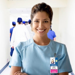 May include: A smiling woman wearing a light blue scrub top and a name tag that reads "General Hospital, Cindy Valencia, Student Nurse". She is standing in a hospital hallway with other medical professionals in the background.