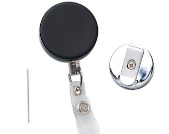 Puede incluir: Un carrete retráctil para credenciales negro con un clip plateado y una correa blanca. El carrete tiene una carcasa de plástico negro y un clip de metal plateado. La correa es blanca y tiene un pequeño botón plateado.