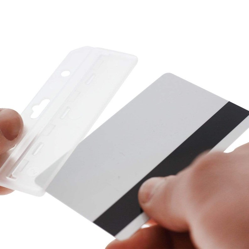 Puede incluir: Un portatarjetas rectangular de pl&aacute;stico transparente con una ranura superior para cord&oacute;n, mostrado mientras se inserta una tarjeta de pl&aacute;stico blanca est&aacute;ndar que presenta una banda magn&eacute;tica negra central para identificaci&oacute;n o acceso.