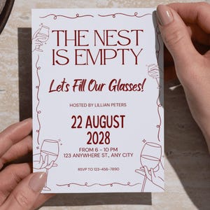 Op de afbeelding: Een witte uitnodigingskaart met bordeauxrode tekst en illustraties. De tekst luidt "THE NEST IS EMPTY" en "Lets Fill Our Glasses!" met evenementdetails. De kaart wordt door handen vastgehouden en bevat de zin "INSTANT DIGITAL DOWNLOAD".