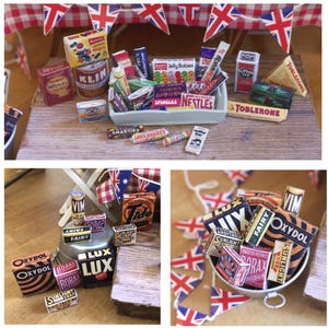 May include: A collection of miniature vintage British food and household product boxes, including Nestlé, Cadbury, and Tide, arranged on a wooden surface. Union Jack flags decorate the background, creating a nostalgic scene.