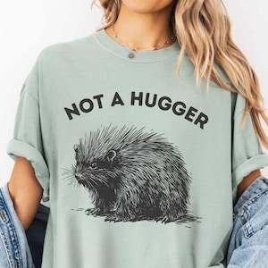 May include: A light green t-shirt featuring a black and white illustration of a porcupine and the text "Not a Hugger".