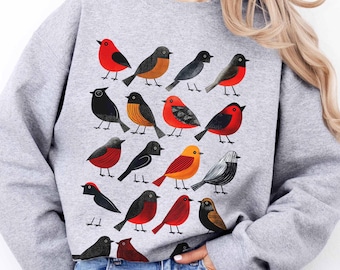 May include: Gray sweatshirt with a colorful bird pattern. The birds are red, orange, black, and white. The sweatshirt has long sleeves and a crew neck.