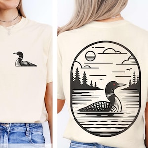 May include: Cream-colored t-shirt featuring a black loon graphic on the front and a larger loon and landscape design on the back. The back design is within an oval frame, with the text "COMFORT COLORS FRONT & BACK DESIGN" at the bottom.