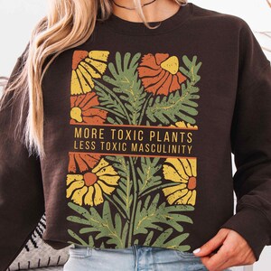May include: Brown sweatshirt with a floral design and the text "More Toxic Plants Less Toxic Masculinity".