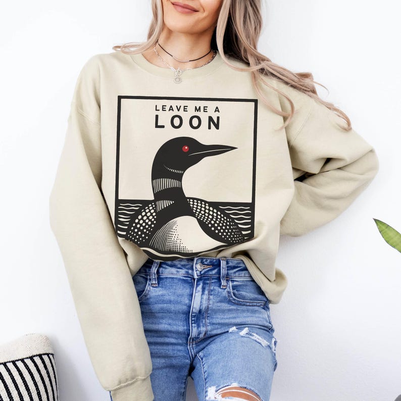 May include: A beige sweatshirt with a black and white graphic of a loon with the text "Leave Me A Loon" printed on the front.