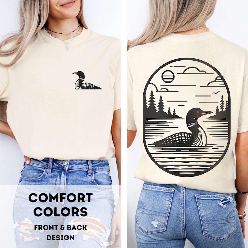 May include: Cream-colored t-shirt featuring a black loon graphic on the front and a larger loon and landscape design on the back. The back design is within an oval frame, with the text "COMFORT COLORS FRONT & BACK DESIGN" at the bottom.