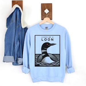 May include: Light blue sweatshirt with a black and white illustration of a loon on the front. The text "Leave me a loon" is printed above the loon.